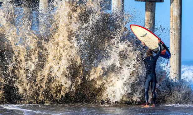 Nathan Barrett of Long Beach raises his surfboard as he gets hit by a large shorebreak wave at the Huntington Beach Pier on Friday morning, January 6, 2023 in Huntington Beach. The recent storm that brought rain, wind and snow to most of California, has also brought large, and in some areas, damaging surf. (Photo by Mark Rightmire, Orange County Register/SCNG)