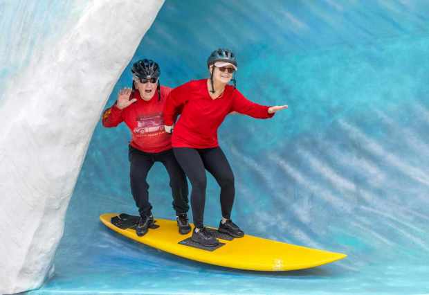 Denny and Monica Asbury of Huntington Beach have their photo taken on a surfboard inside a wave at the International Surfing Museum booth at SURFscape on Saturday, April 29, 2023, in Huntington Beach. Surf and outdoor companies show off their products at booths during the event which took place in a beach-side parking lot along Pacific Coast Highway a few blocks south of the Huntington Beach Pier. (Photo by Mark Rightmire, Orange County Register/SCNG)