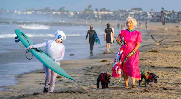 Debby Falese, left, and Jennifer Calonico, both of Huntington Beach, make their way along the beach just north of the Newport Beach Pier early on Saturday morning, October 28, 2023, as surfers wearing a variety of Halloween costumes gather for the annual holiday event of riding the waves in Newport Beach. (Photo by Mark Rightmire, Orange County Register/SCNG)