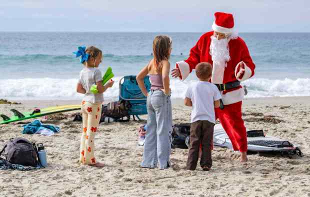 Mike Mitrowski, right, of Laguna Niguel talks with young surfing fans on the beach before competing in the 12th annual Surfing Santa and Stand Up Paddle Board Contest held at Salt Creek Beach in Dana Point on Saturday, November 18, 2023. The event benefits Surfers Healing, a surf camp for children with autism. (Photo by Mark Rightmire, Orange County Register/SCNG)