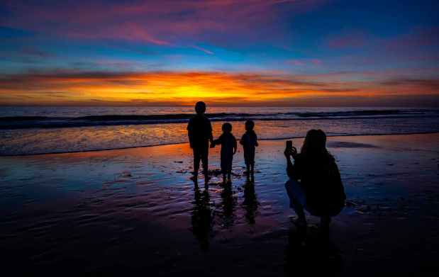Tara Iwata, right, of Costa Mesa takes a photo of Axel Simmons, 9, left, and her two sons, Cru, 4, center, and Slater, 3, as the sun sets at Crystal Cove State Park in Newport Beach on Saturday, December 2, 2023. The group attended Crystal Cove Conservancy's annual tree lighting ceremony and holiday bazaar on the beach. (Photo by Mark Rightmire, Orange County Register/SCNG)