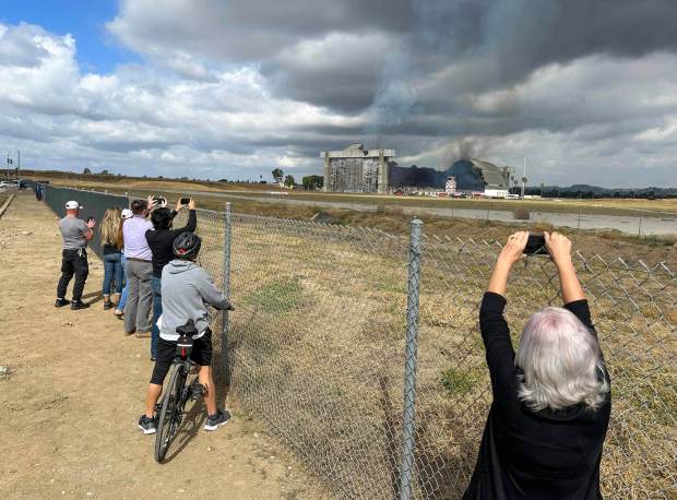 People stand along Warner Avenue as they watch firefighters work to control a blaze at the north blimp hangar at the former Marine Corps Air Station Tustin in Tustin, CA, on Tuesday, Nov. 7, 2023. (Photo by Jeff Gritchen, Orange County Register/SCNG)