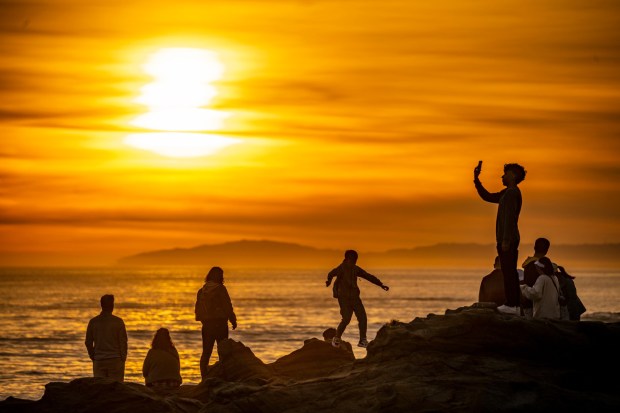 People gather on the rocks at sunset seen on the beach below Heisler Park to watch the sunset in Laguna Beach on Thursday, January 12, 2023. (Photo by Leonard Ortiz, Orange County Register/SCNG)